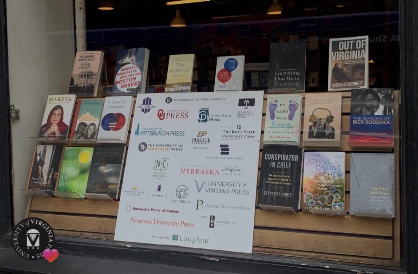 The Harvard Book Store window displaying university press titles around a Longleaf Services sign, with Out of Virginia by Joseph P. Stinnett in the upper right.